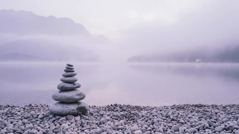 Aufeinandergeschichtete Steine am Ufer eines Sees, dahinter liegt dichter Nebel.