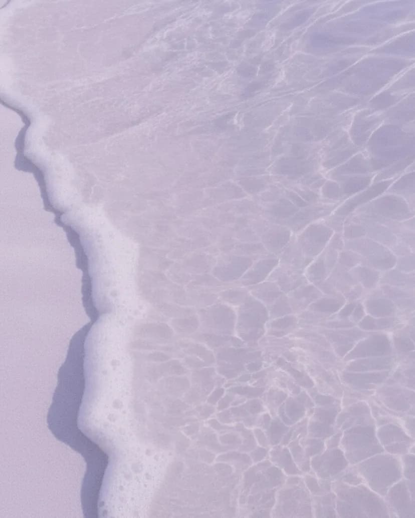 Eine Welle läuft auf hellem Sand aus, die Wasserkante zieht eine feine Linie.