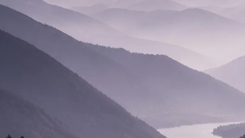 Bergketten im Morgennebel, ein Fluss zieht ruhig durch das Tal.