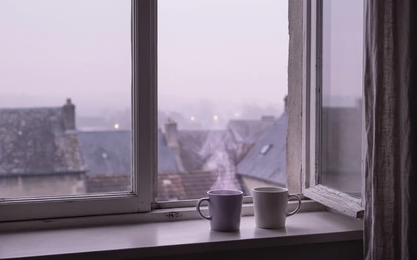 Zwei Tassen auf einem Fenstersims, draussen dämmert der Morgen über den Dächern.